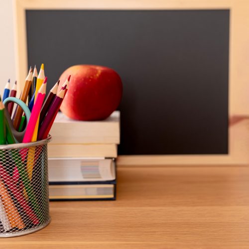 apple on school books with pencils on desk and empty blackboard - back to school